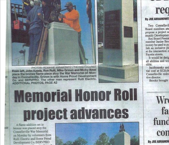 A Newspaper Clipping of a SERVPRO employee placing bronze flame piece on top of a memorial in our sister franchise in Fayette
