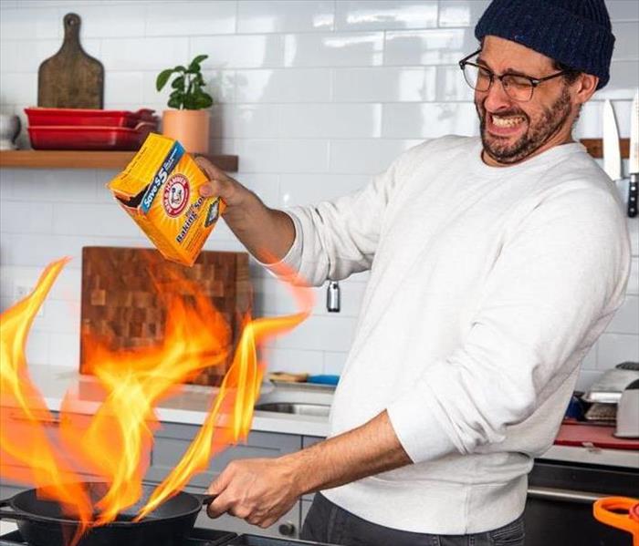 A Picture of a man trying to put out a grease fire with baking soda. 